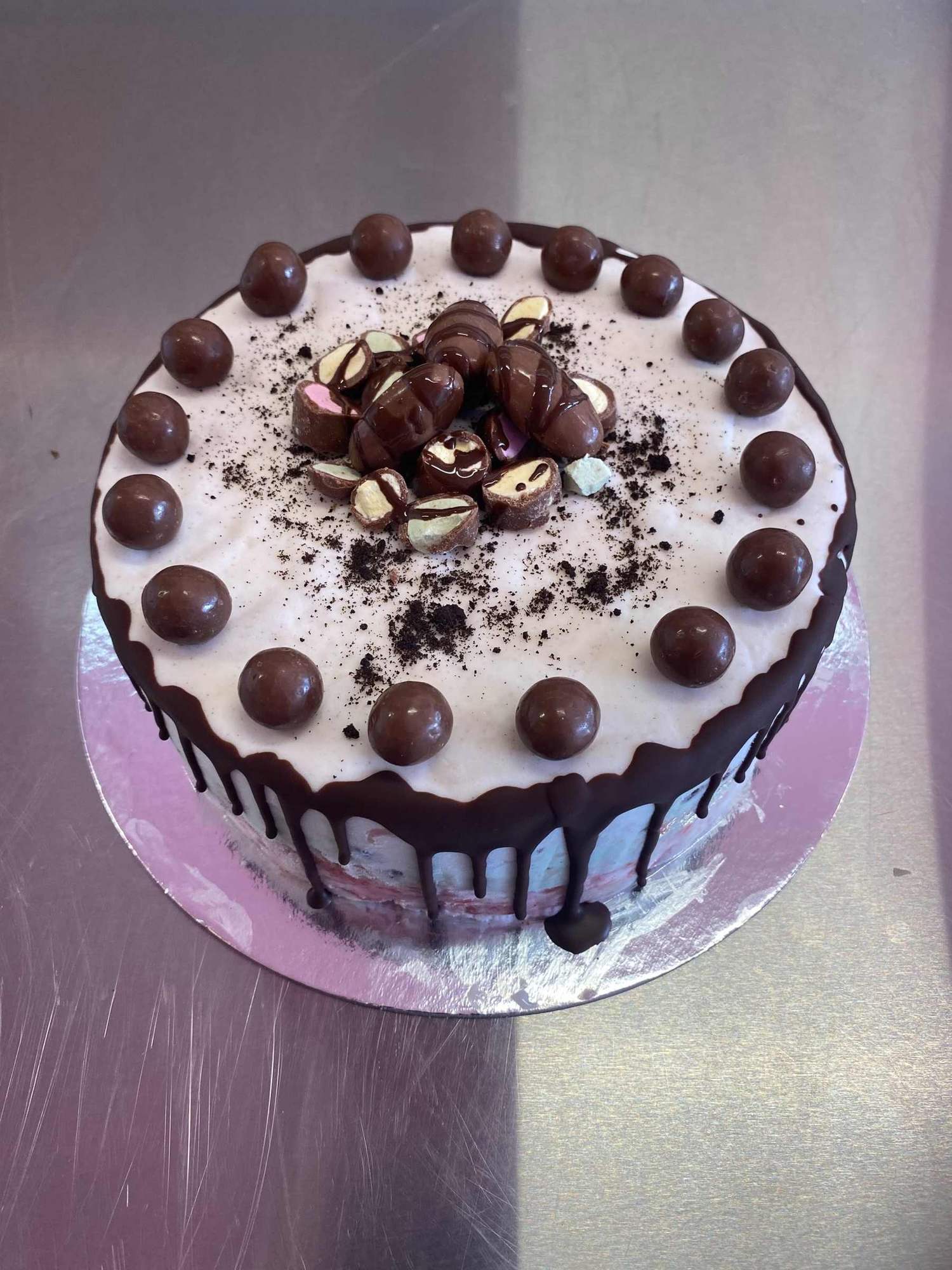 A white gelato cake with chocolate drip and chocolate balls on top