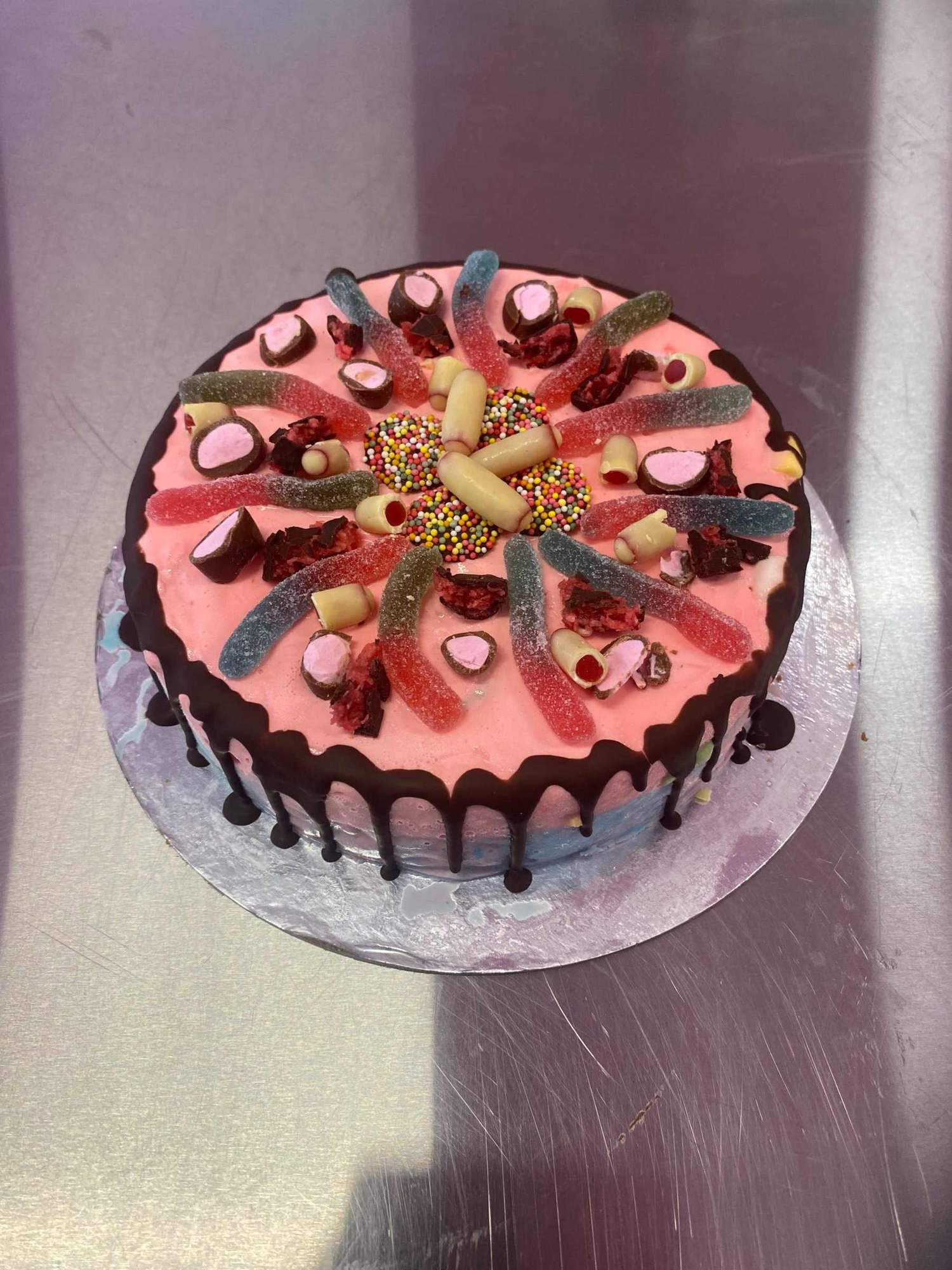 A pink gelato cake with sour lollies and chocolate drip