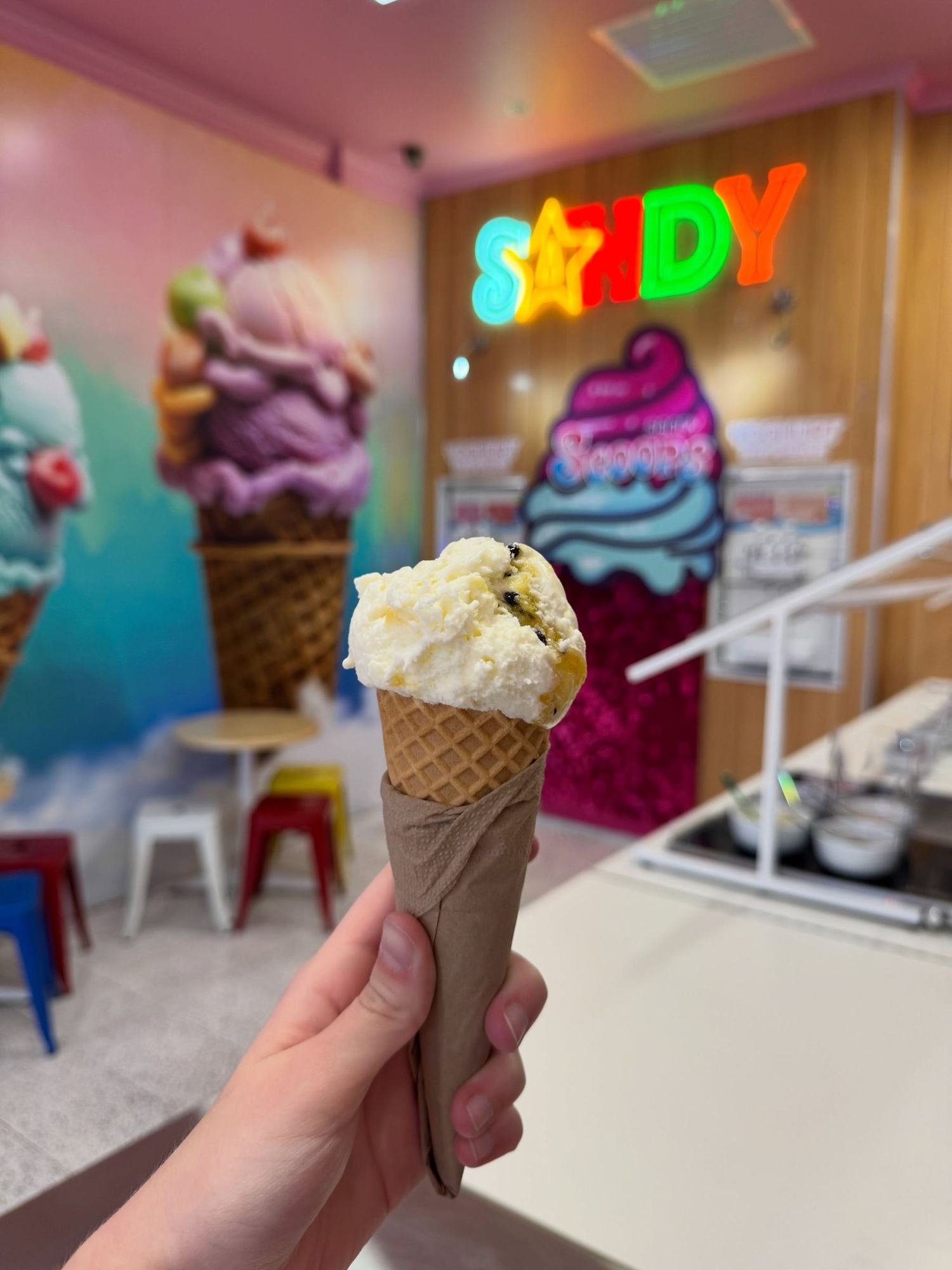 A vanilla gelato waffle cone held in front of the sign