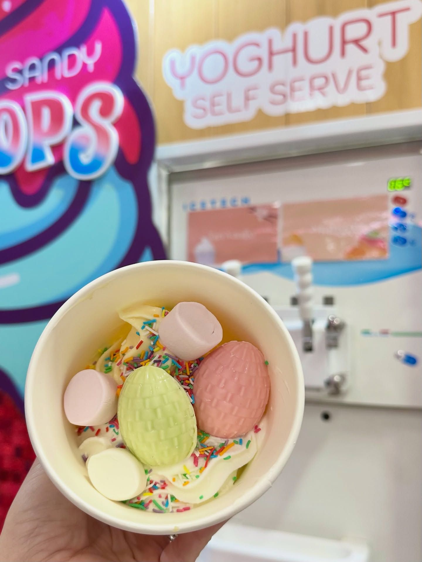 A cup of frozen yoghurt topped with marshmallows and sprinkles
