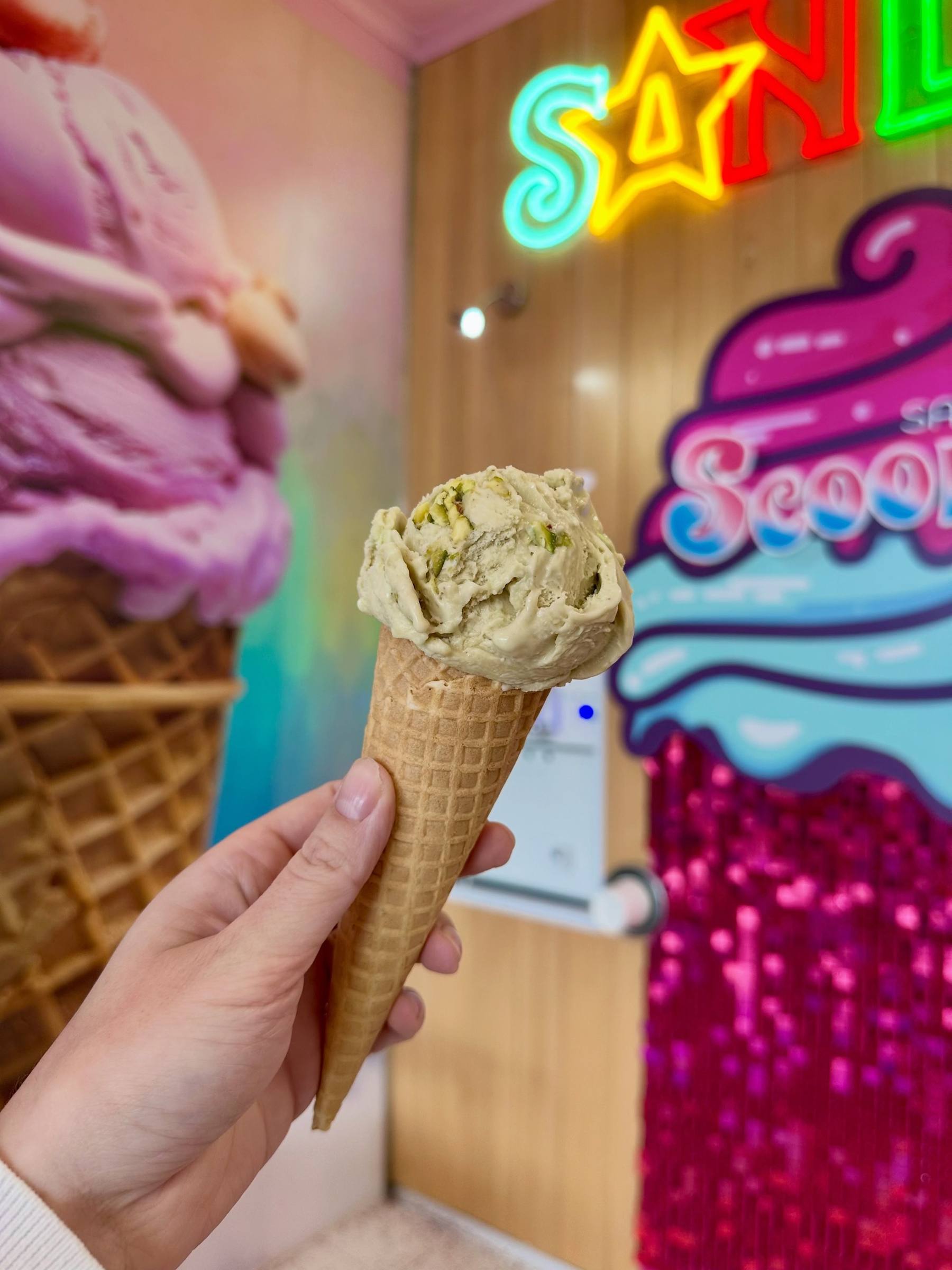 A pistachio gelato cone in front of the sequin wall