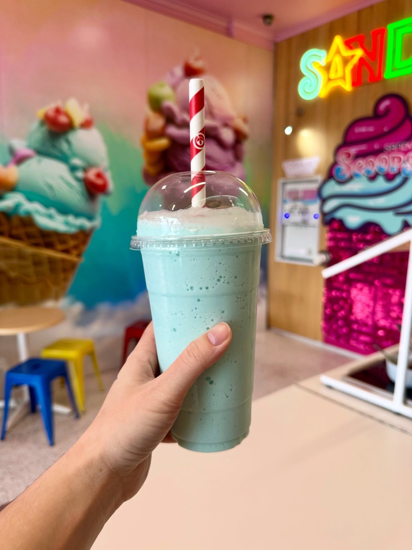 A blue milkshake held up in front of the neon sign